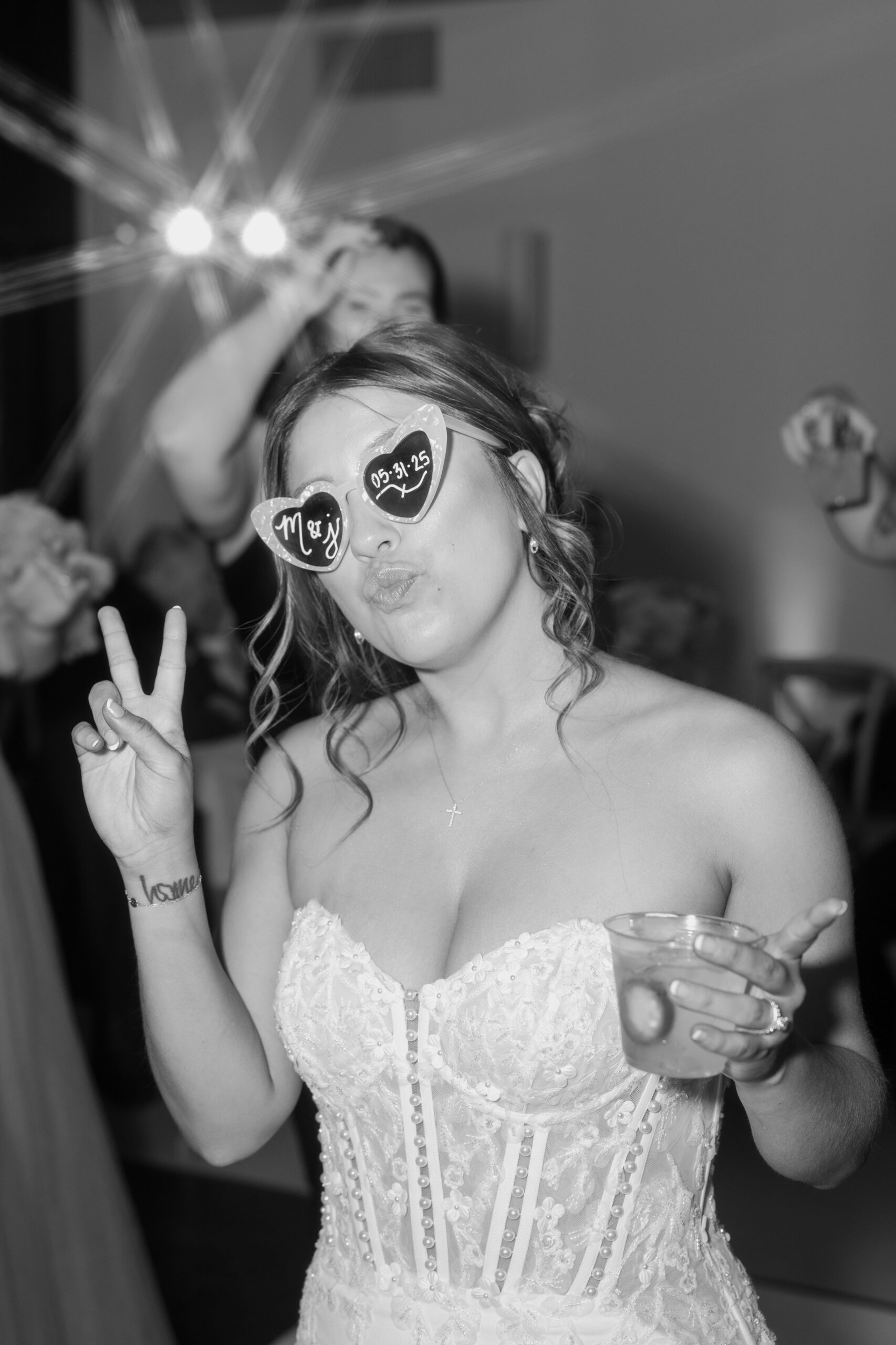 Bride wearing heart-shaped sunglasses with the couple’s initials and wedding date while holding a drink and posing on the dance floor at a Desert View wedding.