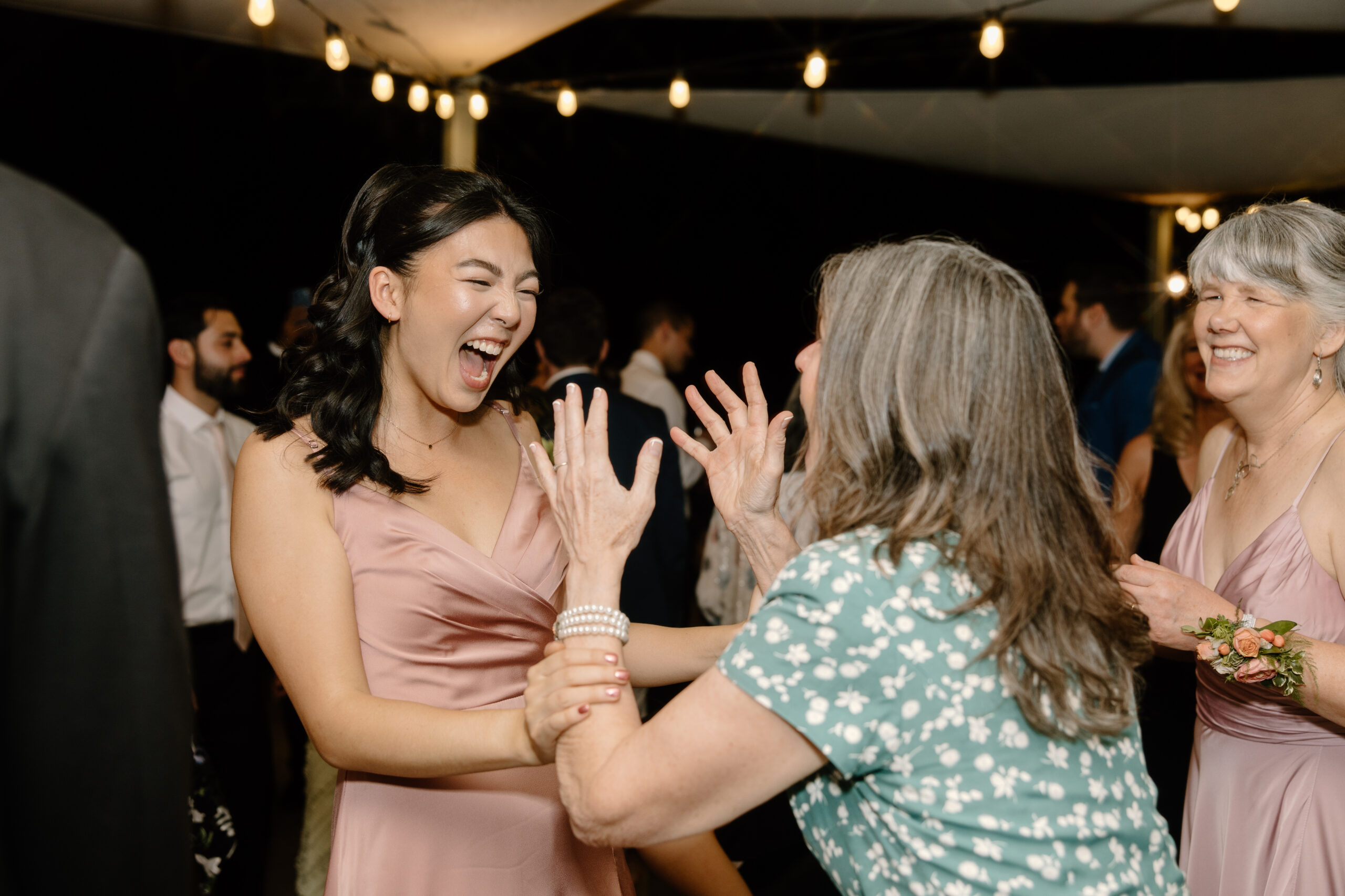 Guests dancing together on the dance floor, laughing and celebrating under string lights