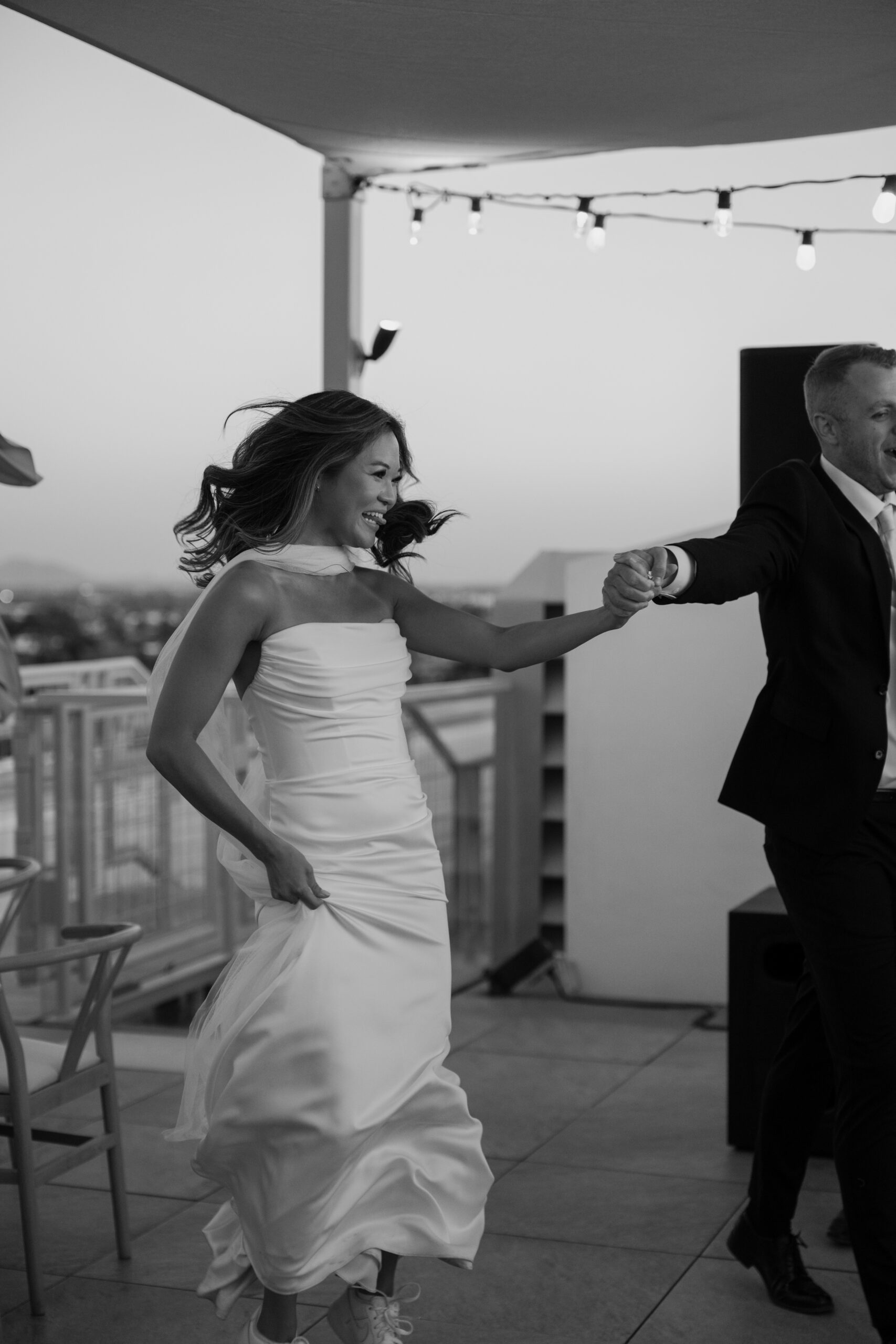 Black and white photo of bride dancing and twirling during the reception while holding her dress