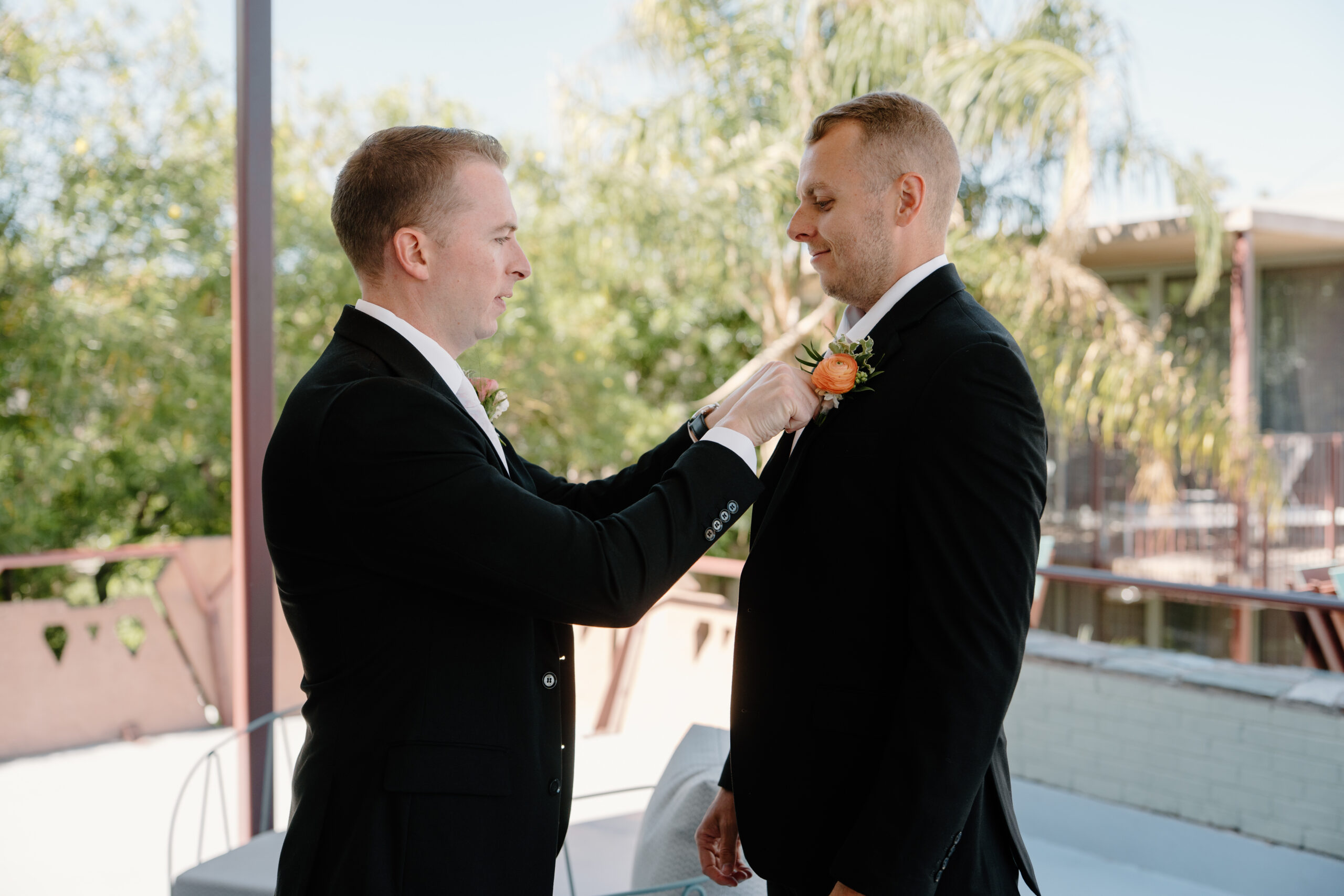 Groomsman adjusting the groom’s boutonniere on a balcony before the ceremony at Hotel Valley Ho