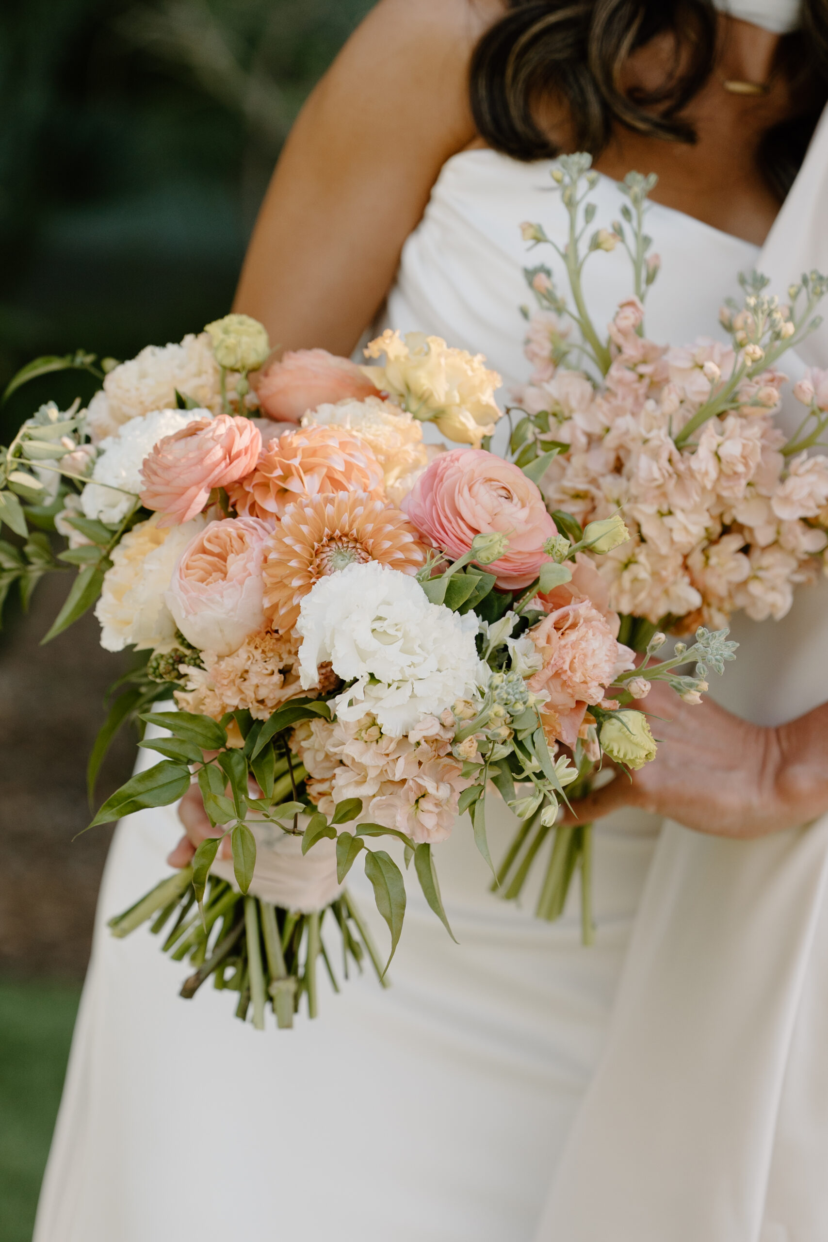 Close-up of a bride holding a soft peach and white bouquet with delicate garden-style florals