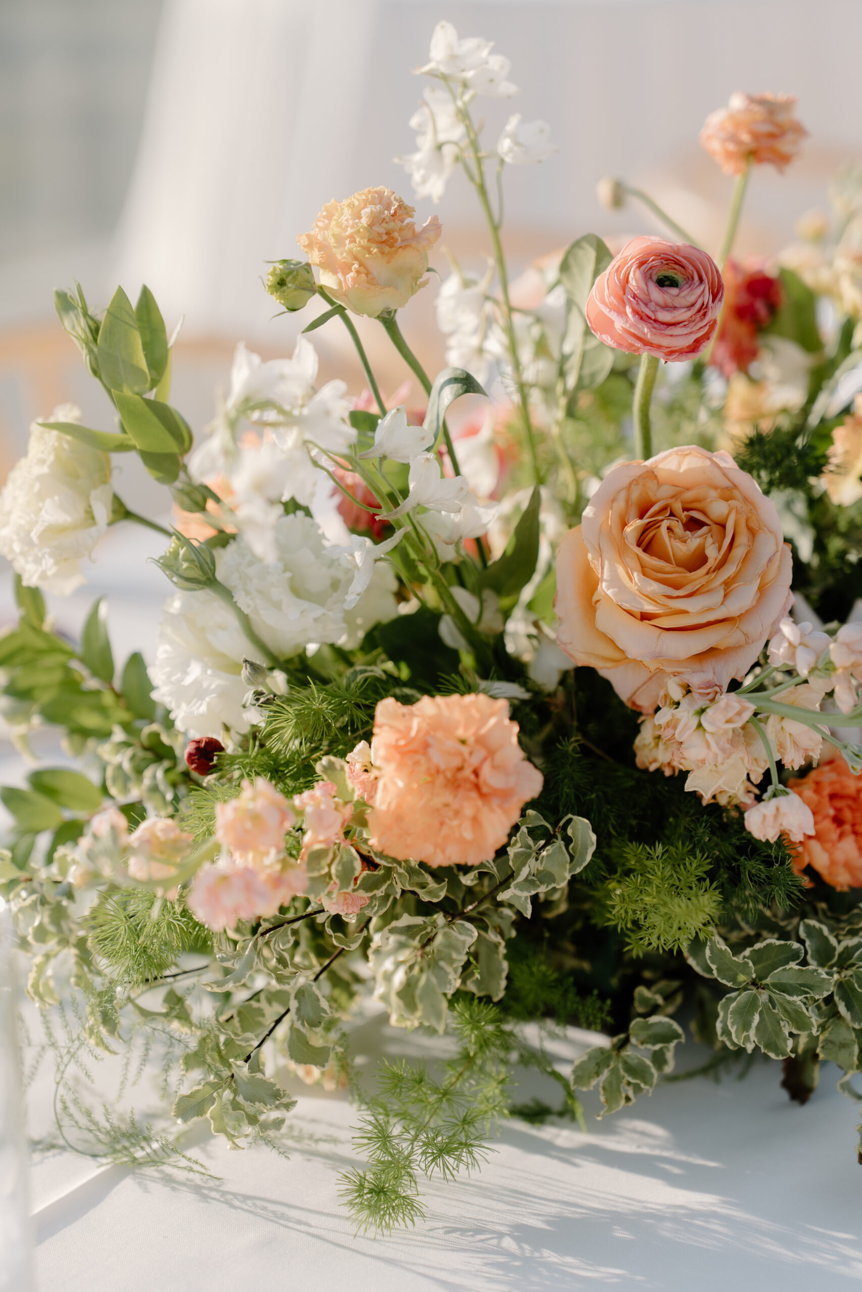 Light and airy floral centerpiece featuring peach roses, ranunculus, and greenery arranged in soft natural light