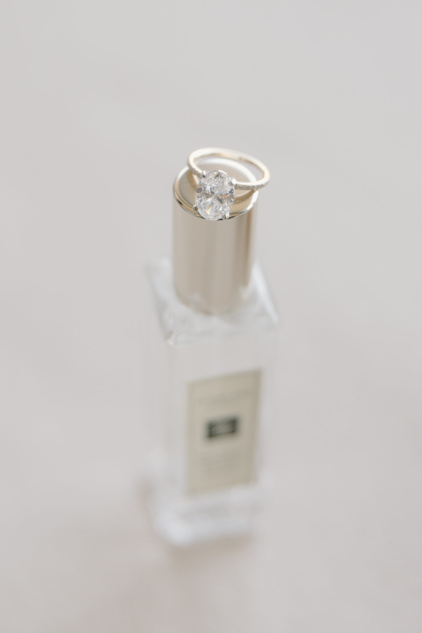 Elegant engagement ring resting on top of a perfume bottle with soft, minimal styling