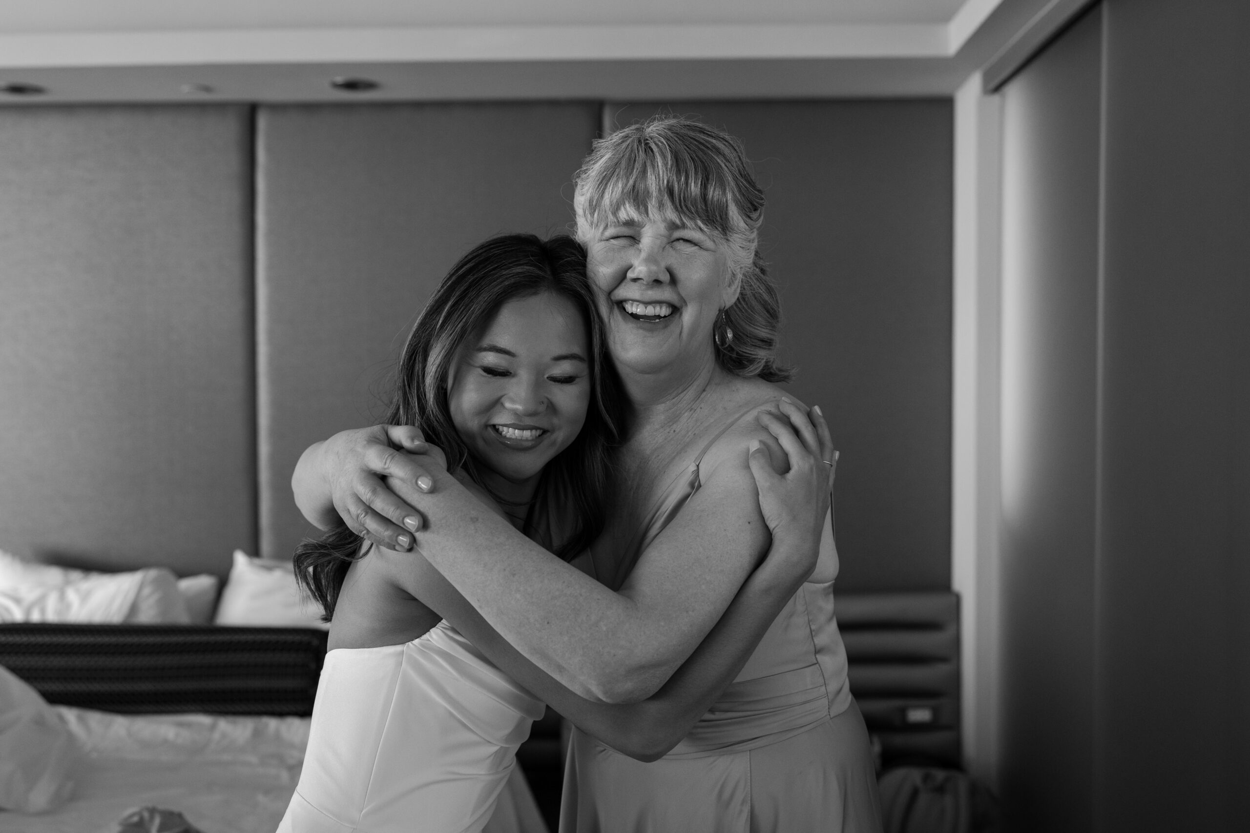 Emotional black and white moment of bride hugging an older woman, both smiling during getting ready