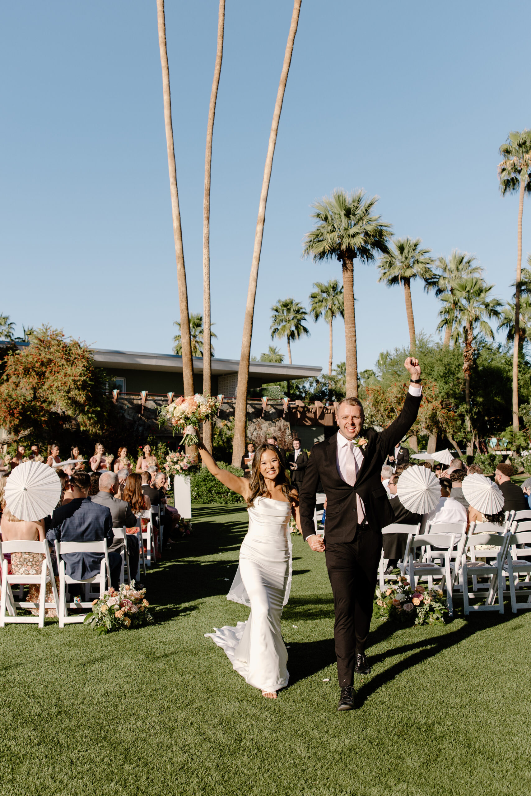 Bride and groom walking down the aisle smiling and celebrating after their ceremony with guests cheering behind them