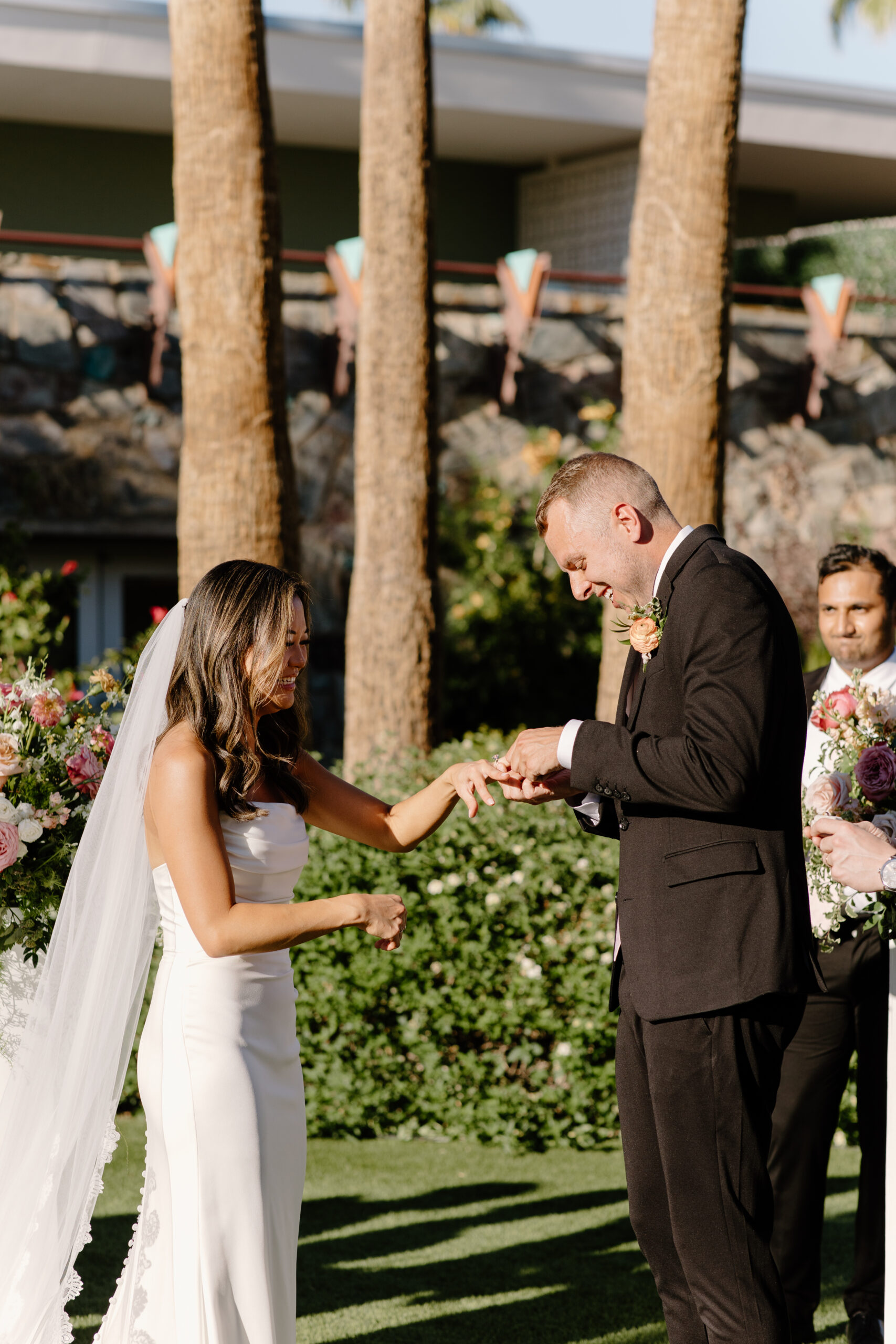 Bride and groom exchanging rings during an outdoor ceremony at Hotel Valley Ho, surrounded by palm trees and greenery