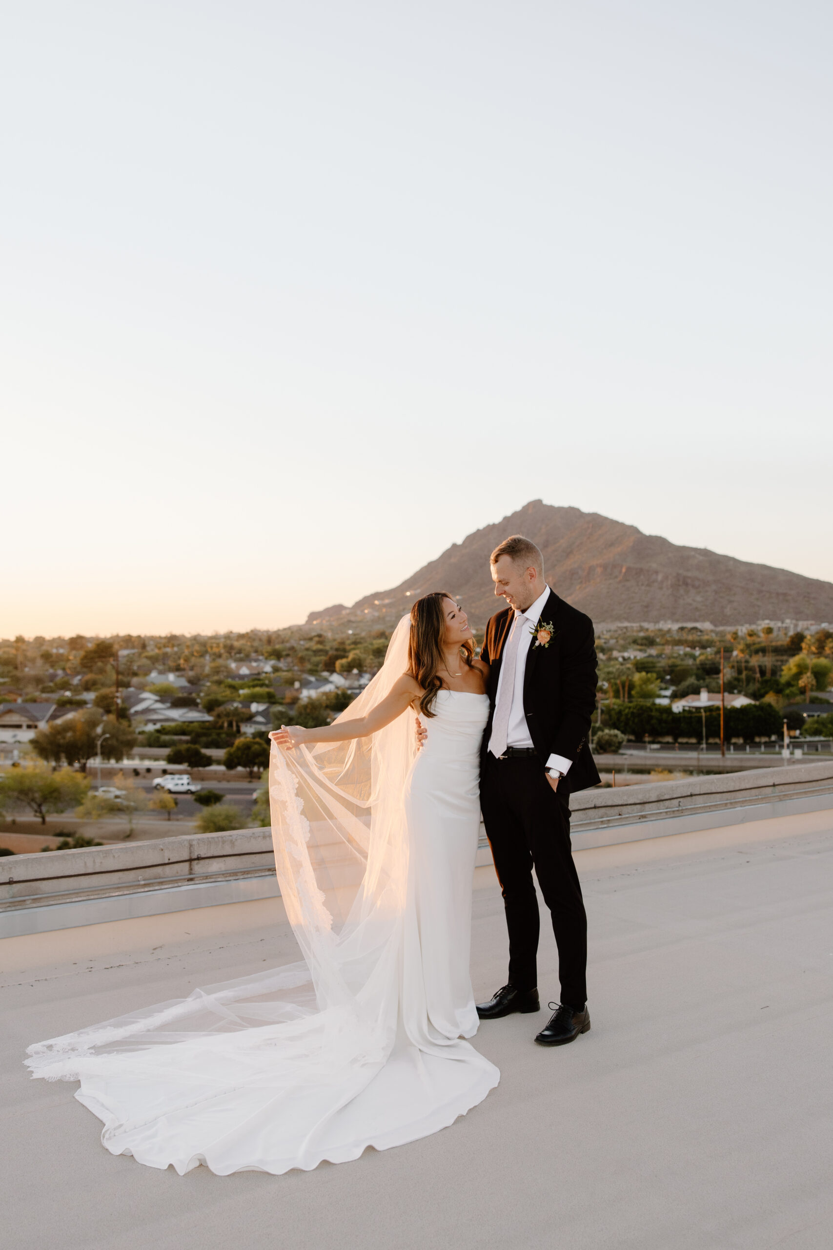 Bride and groom standing together on a rooftop at sunset with mountain views in the background