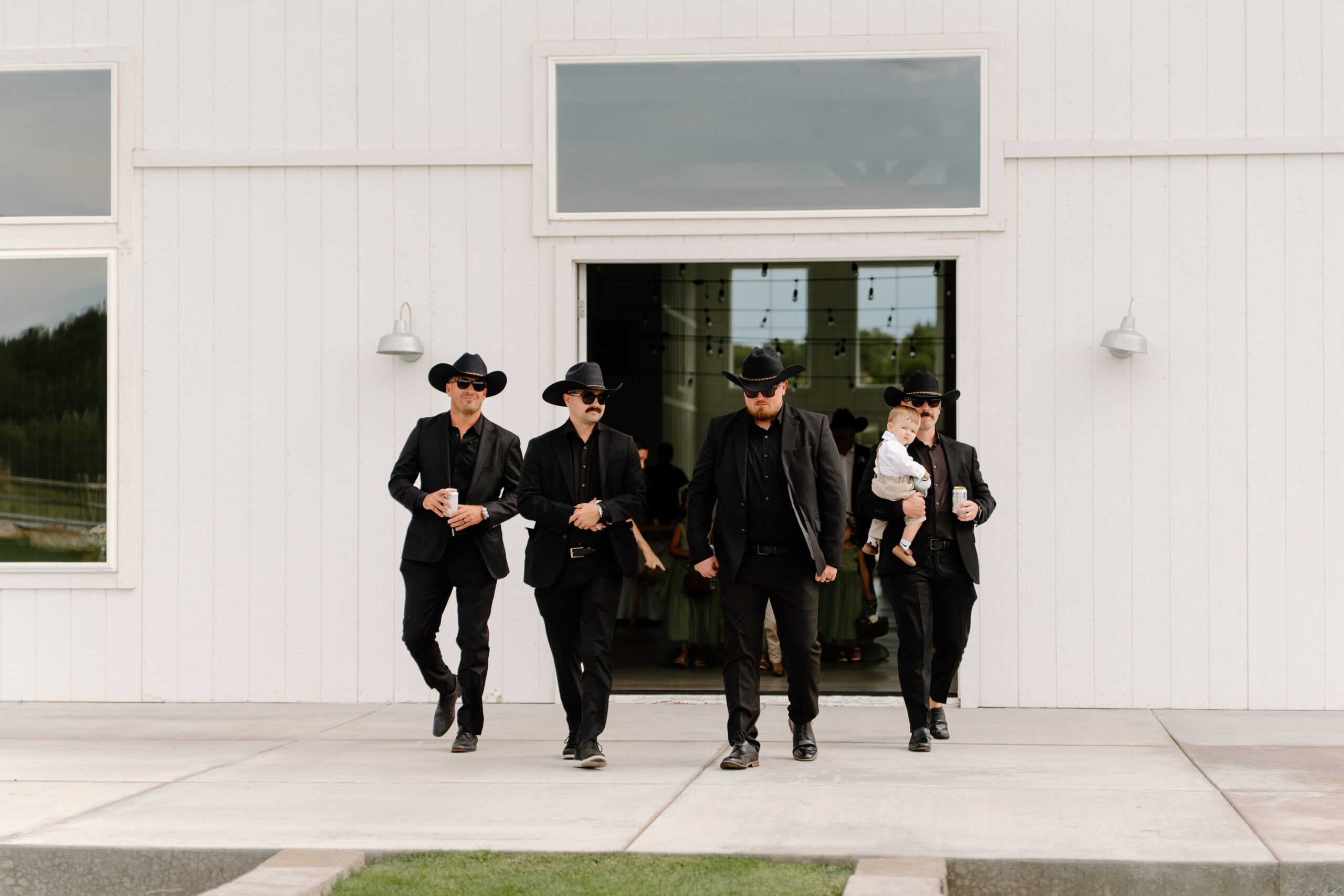 Groomsmen in black western-inspired attire making their entrance outside the wedding venue