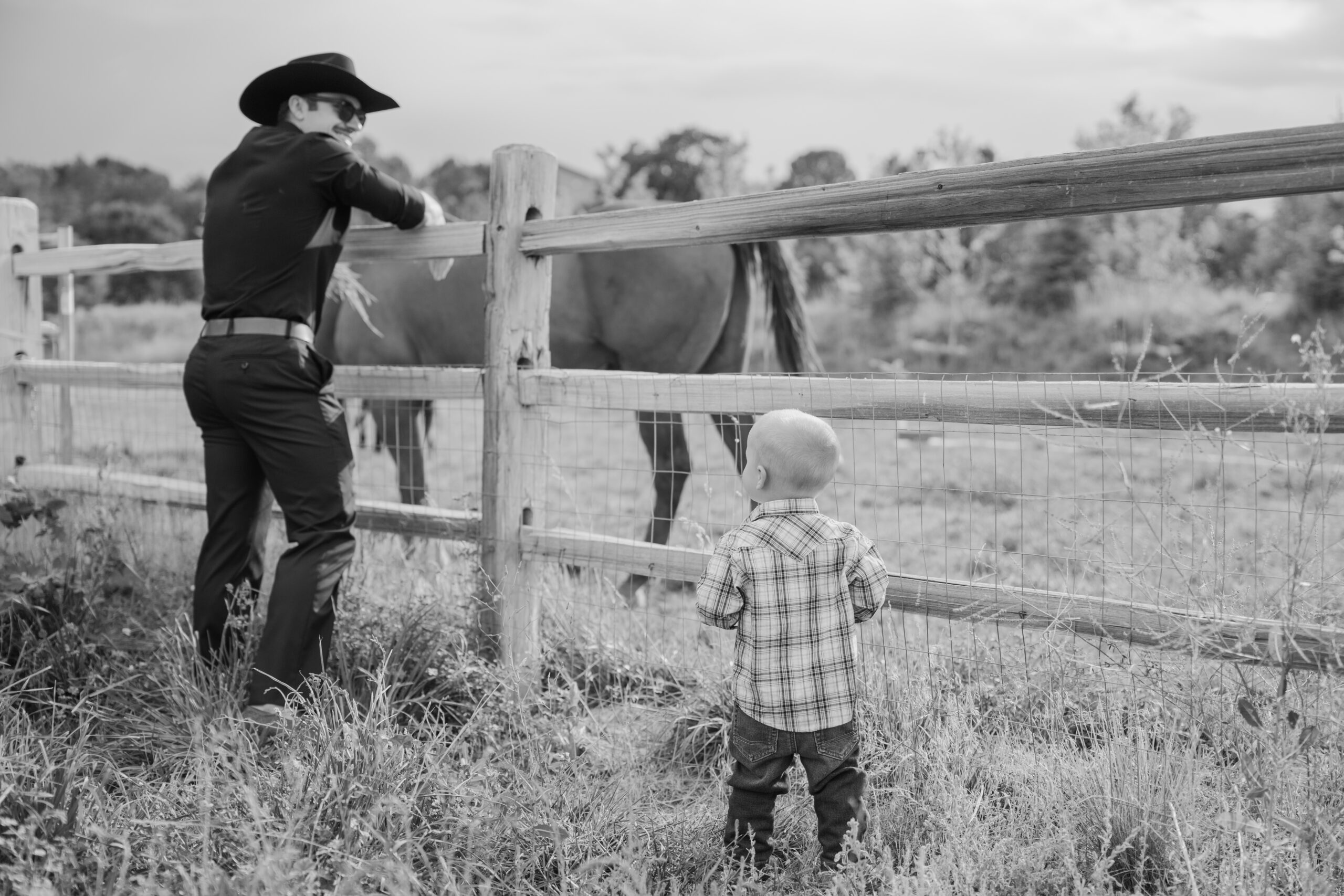 Black and white candid of a child and wedding guest standing by the fence watching a horse