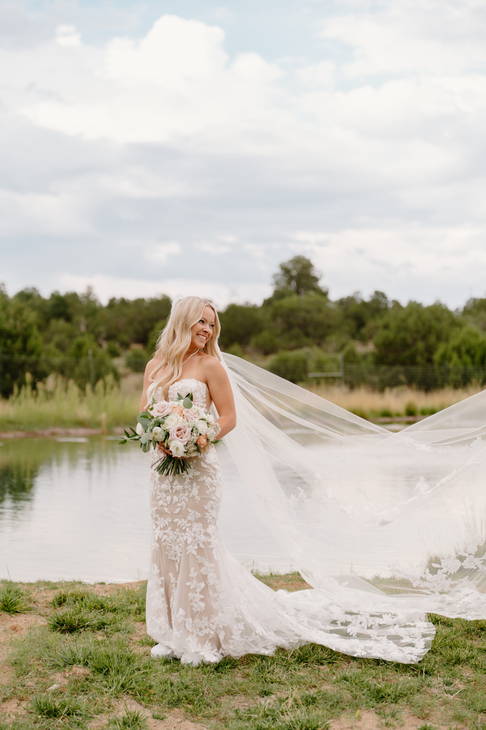 Bridal portrait by the water with flowing veil and soft floral bouquet at The Sycamore, Flagstaff
