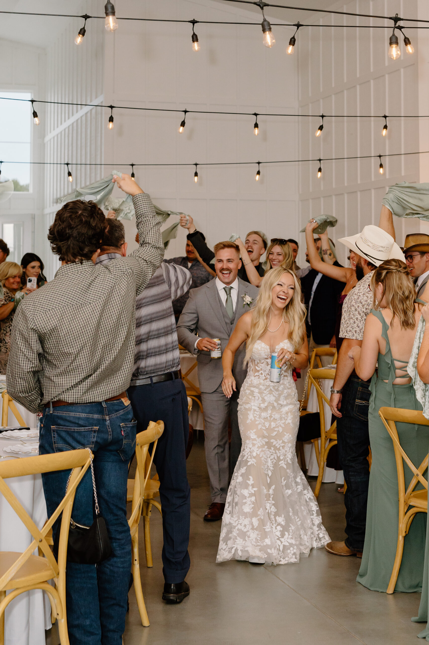 Bride and groom making their reception entrance while guests wave napkins and celebrate indoors