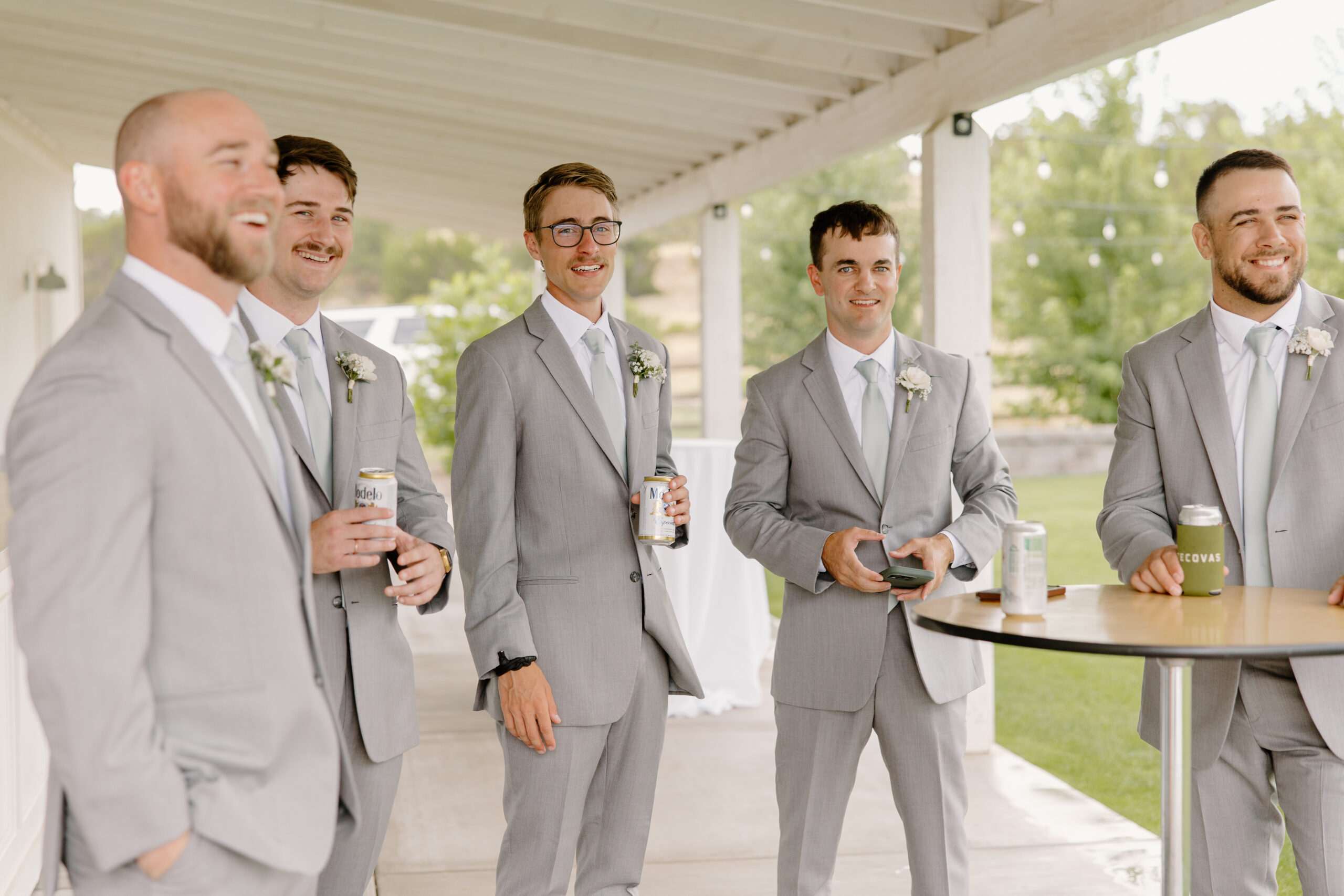 Groomsmen in light gray suits sharing drinks and laughing together before the ceremony at The Sycamore, Flagstaff