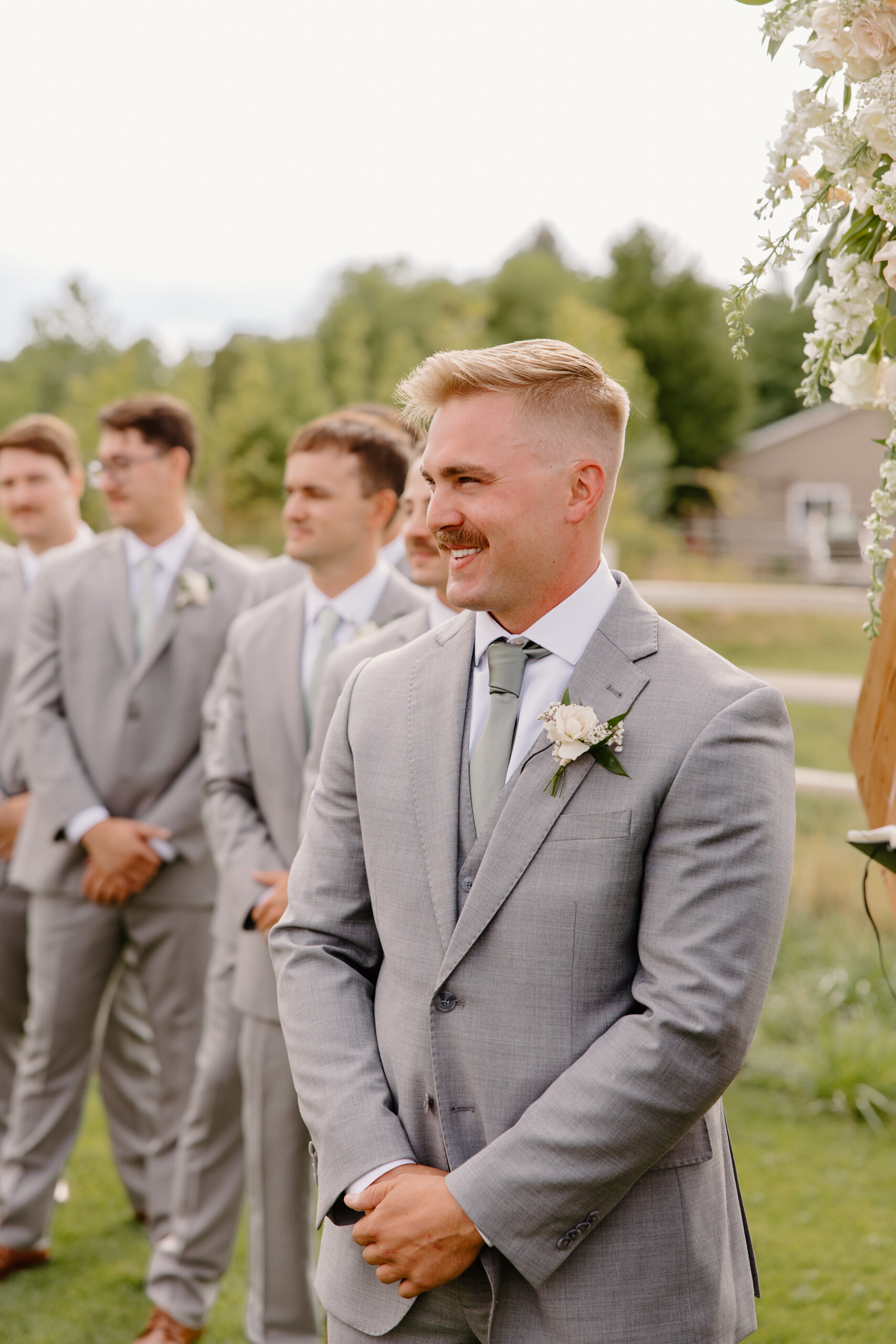 Groom smiling during the wedding ceremony while standing with his groomsmen outdoors