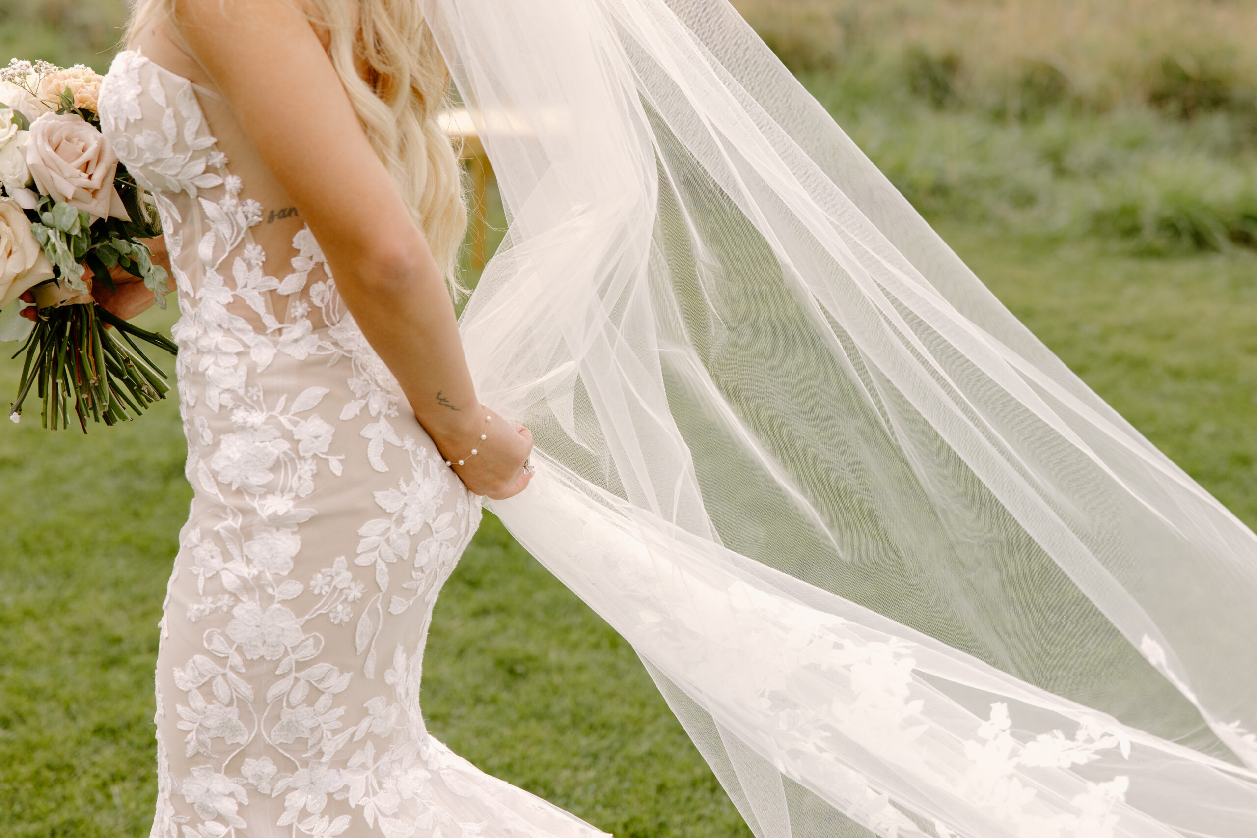 Close-up detail photo of the bride’s lace wedding dress and flowing veil outdoors at The Sycamore, Flagstaff