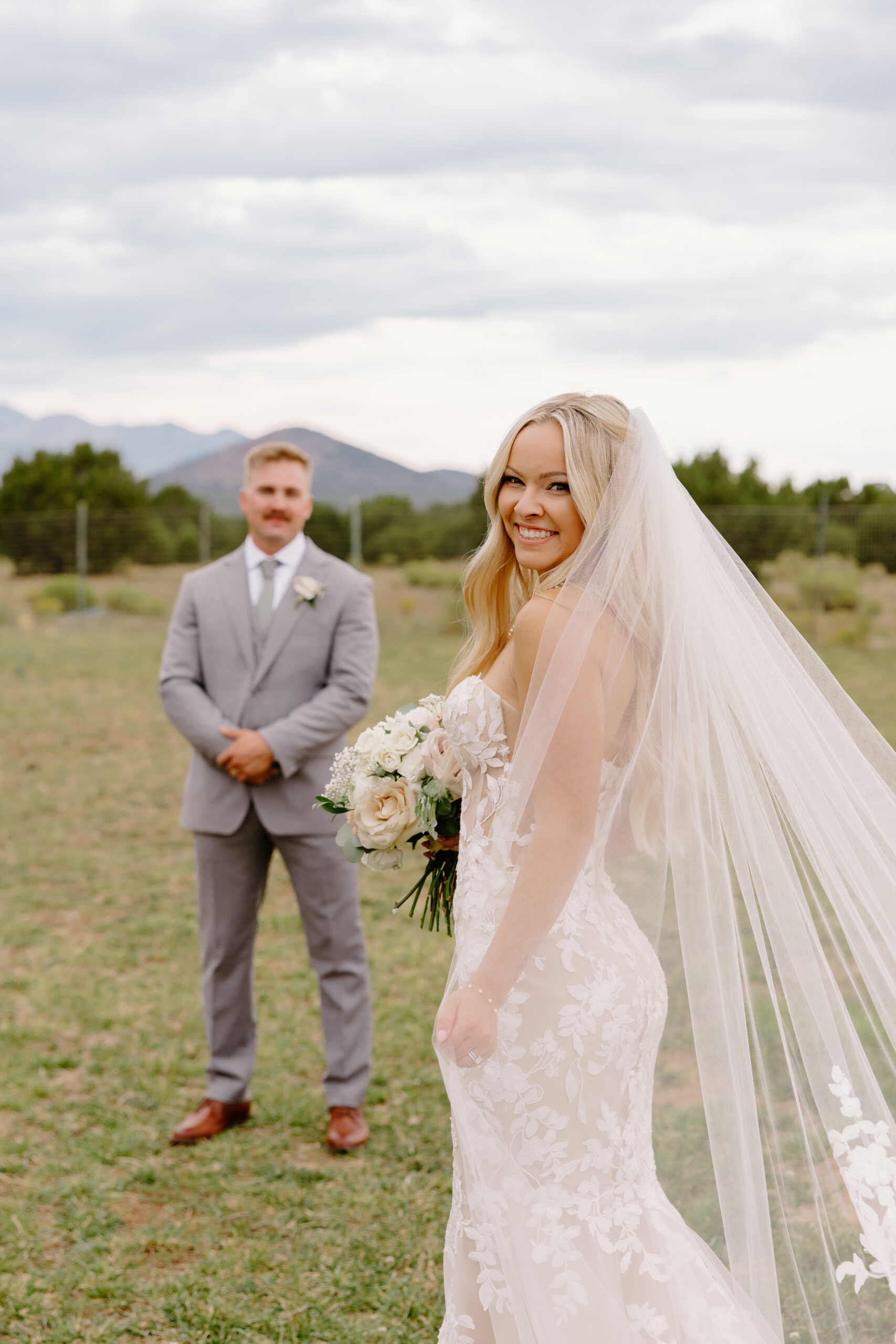 Bride smiling during a first look with her groom in an open field with mountain views near The Sycamore, Flagstaff