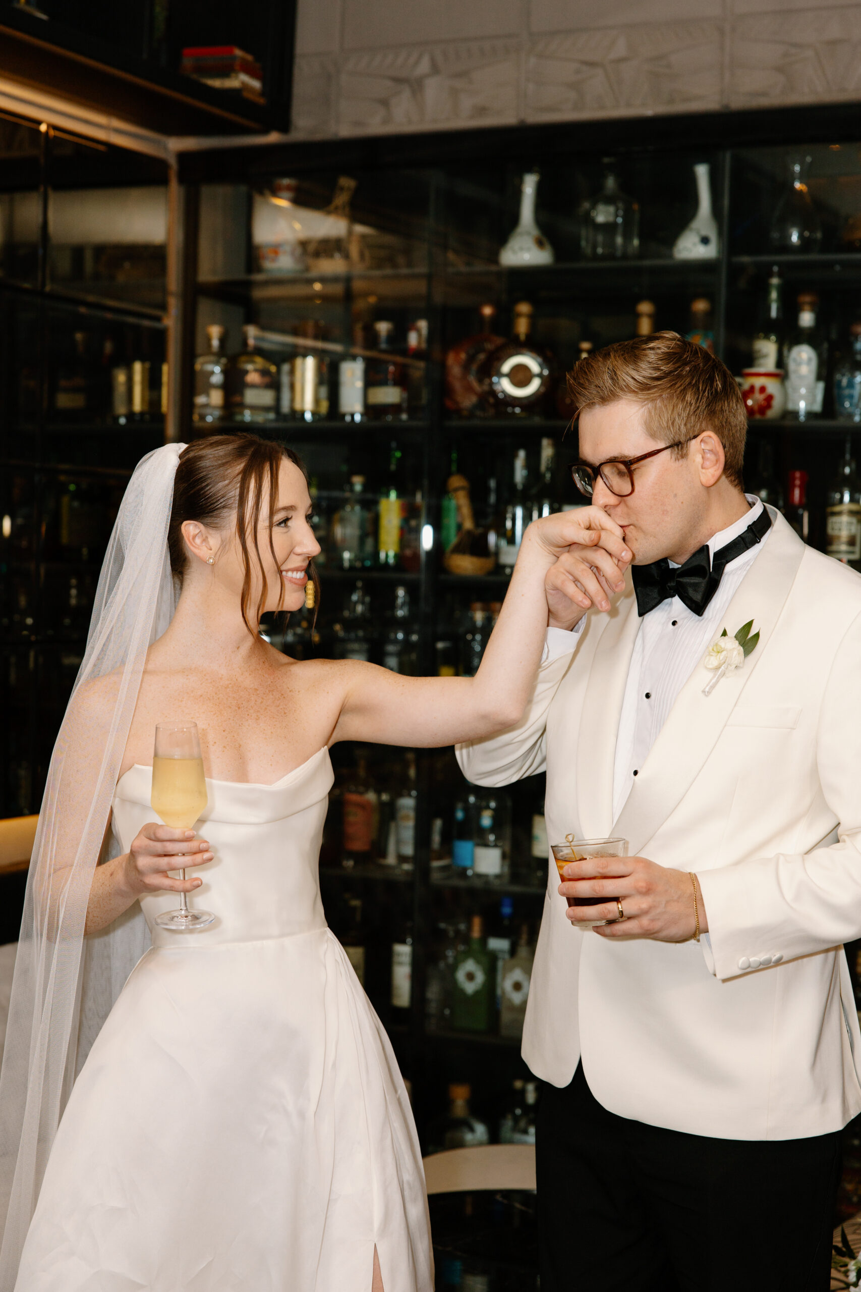Groom kissing the bride’s hand while they enjoy cocktails together at the bar.