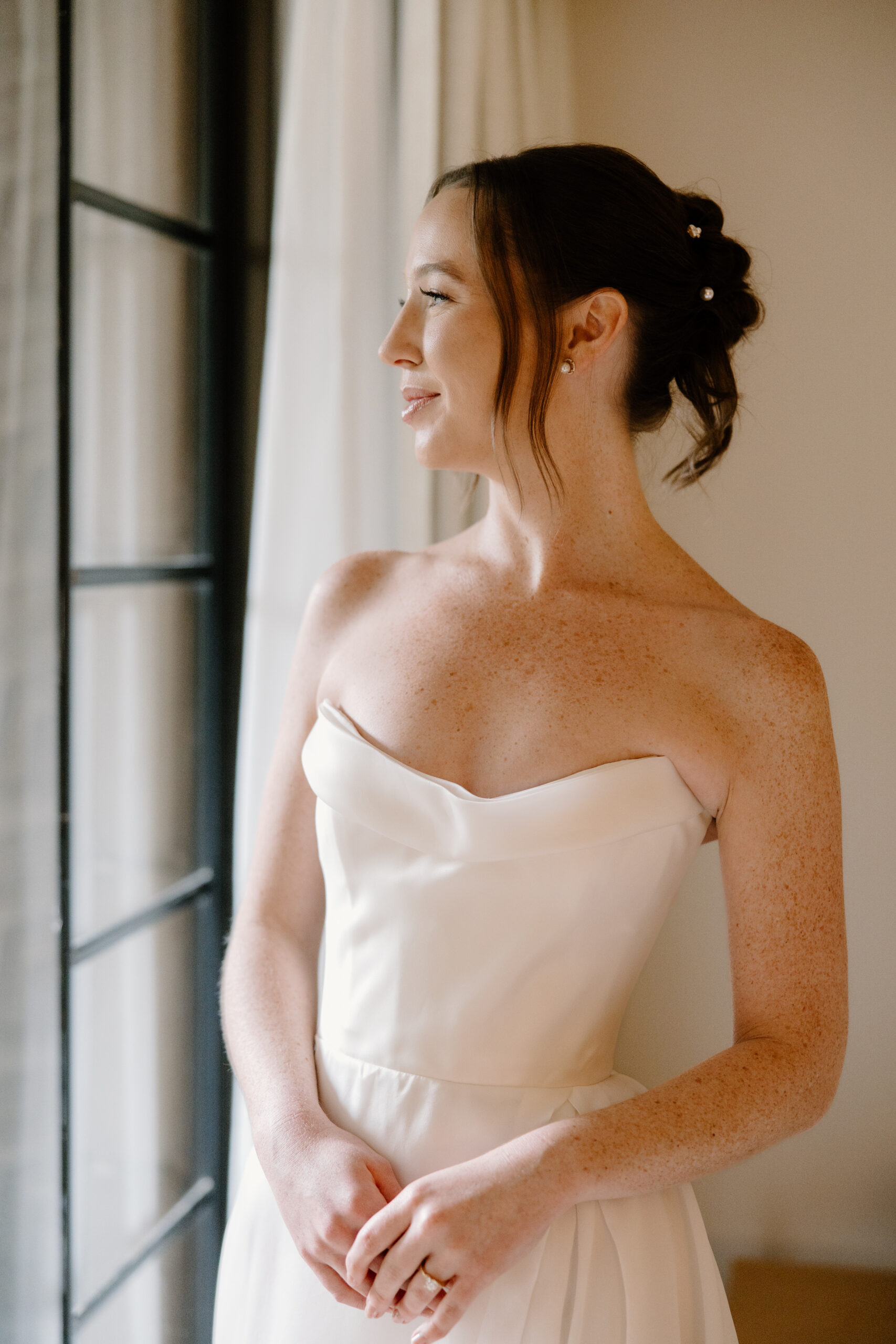 Bride in her strapless wedding gown standing beside a window while getting ready at the Arizona Biltmore.