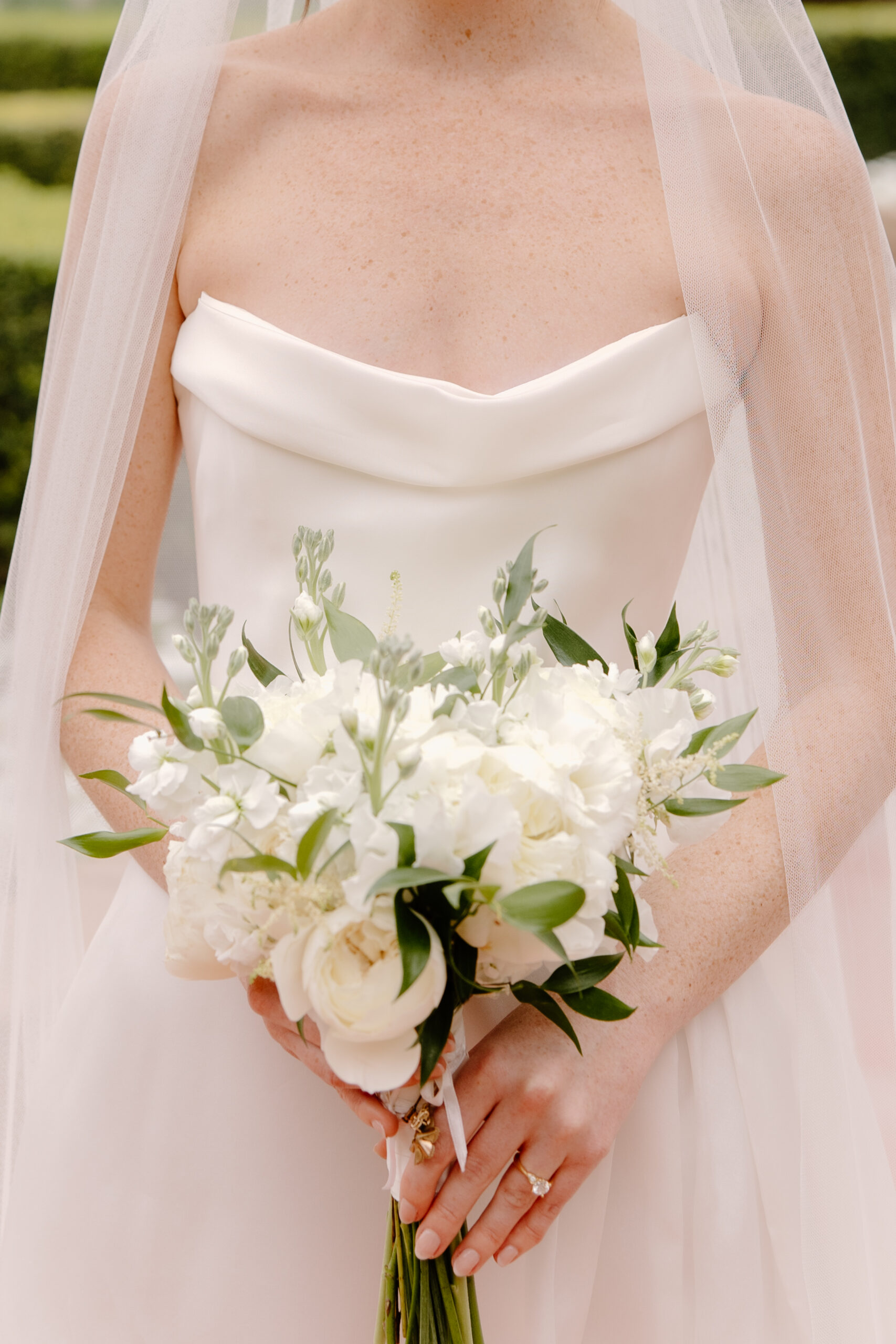 Close-up of the bride holding a white and green wedding bouquet against her classic satin gown.