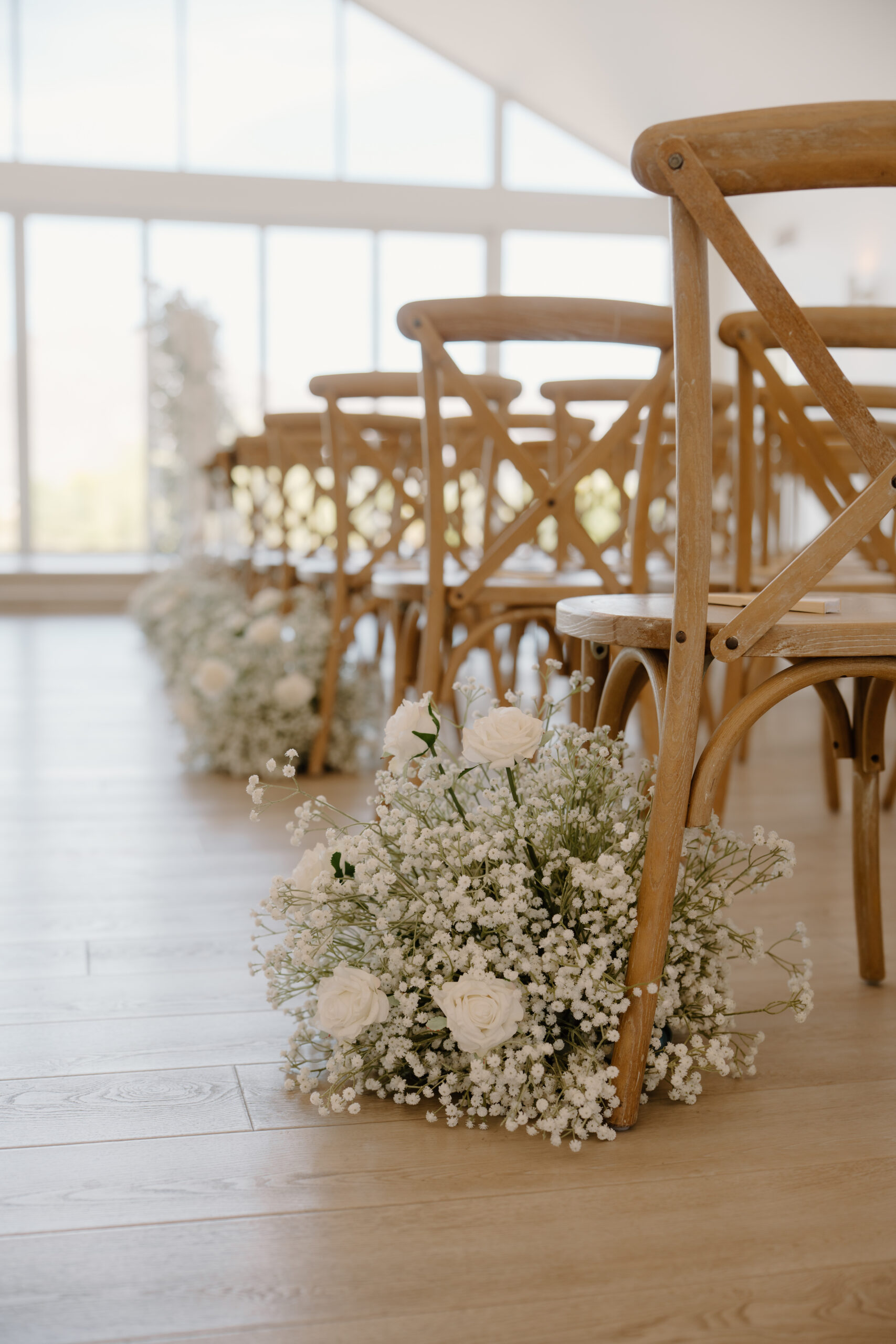 A photo of aisle markers containing babies breathe and white roses placed next to wooden ceremony chairs.