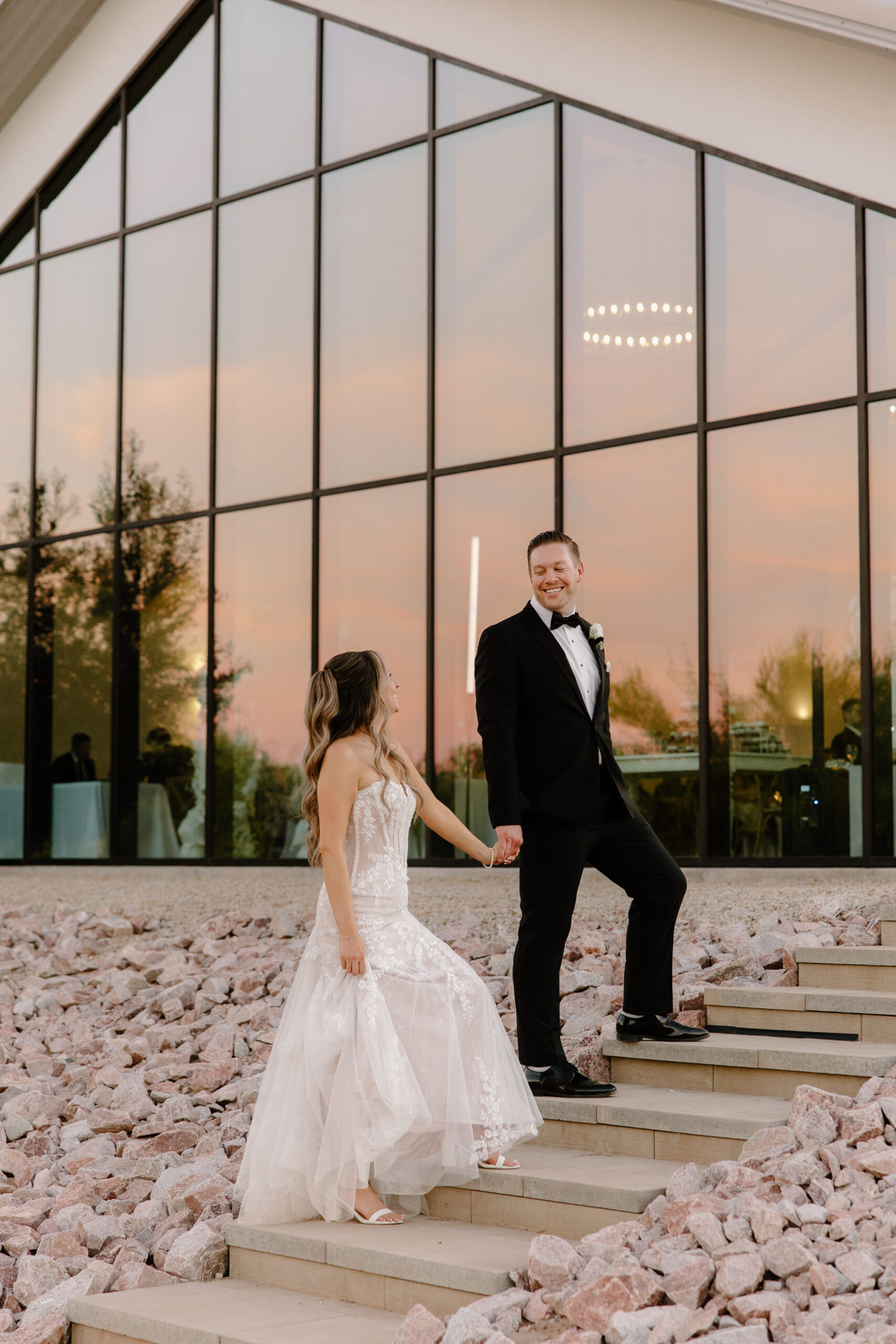 An outdoor portrait of a bride and groom smiling at each other on the stairs.