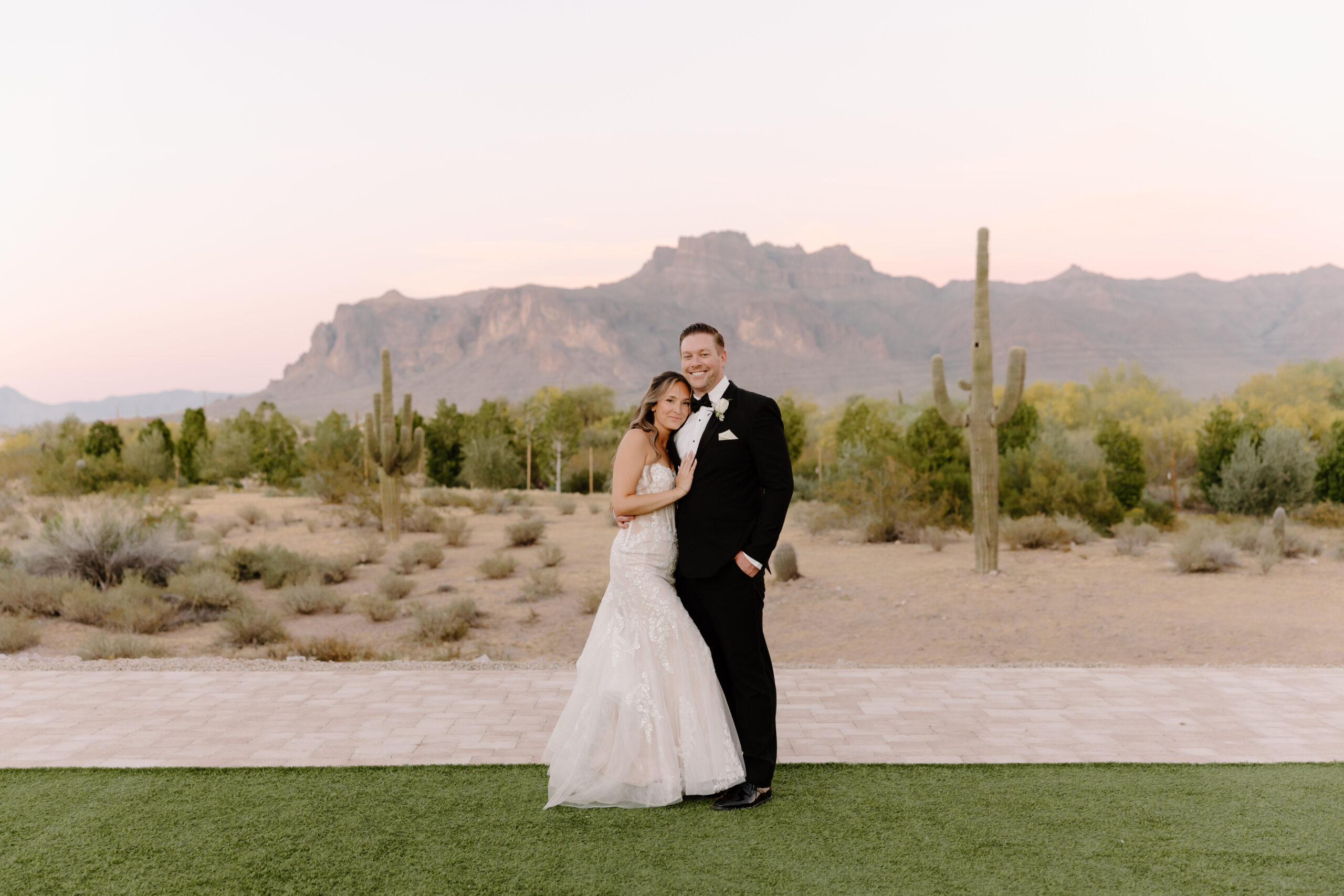 Bride and groom posing in the Arizona desert with saguaros and dramatic mountain views behind them.