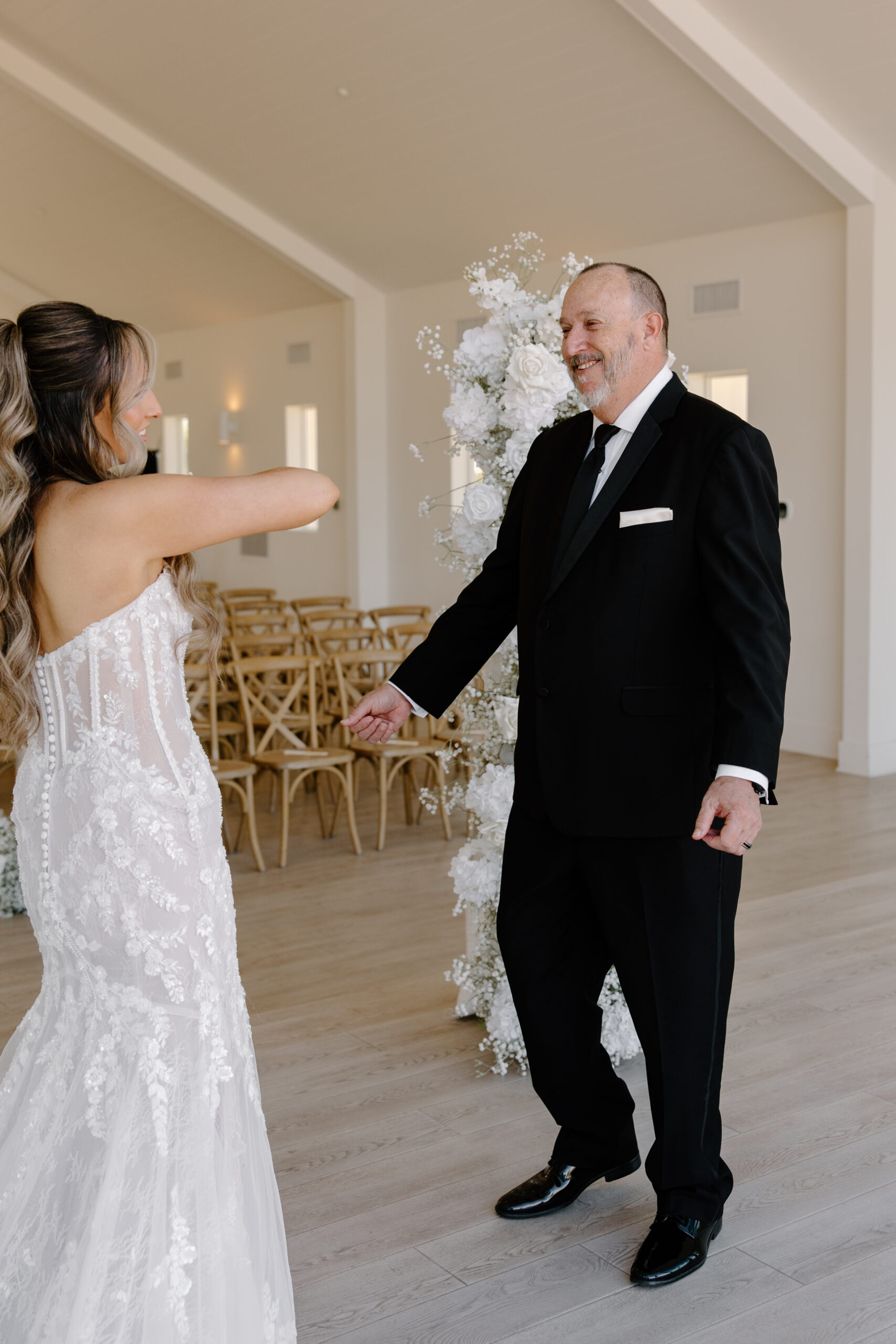 Bride seeing her father before the ceremony as he smiles and reaches toward her inside the bright wedding venue.