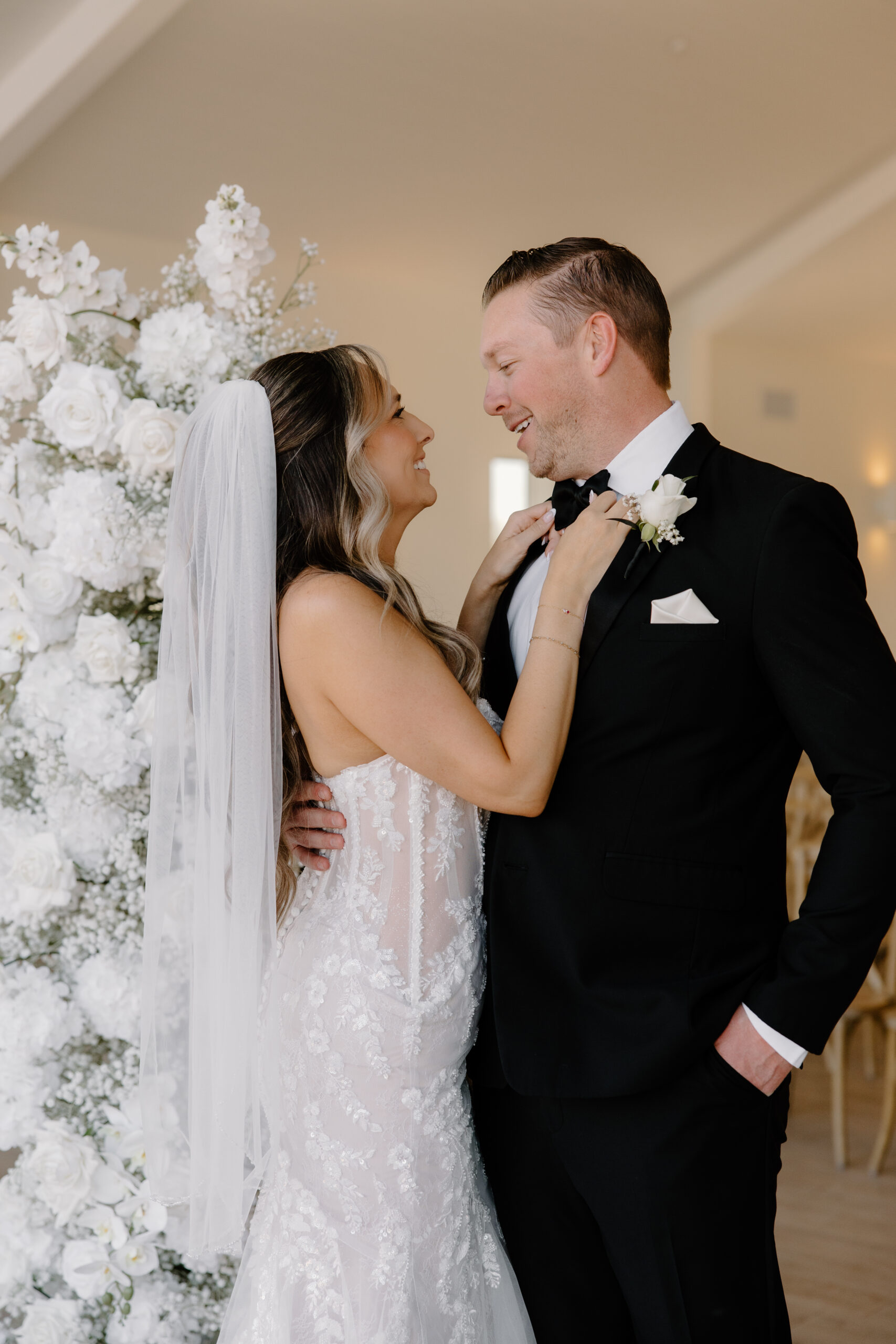 Bride and groom smiling at each other beside a white floral ceremony installation, captured by an Arizona wedding photographer.
